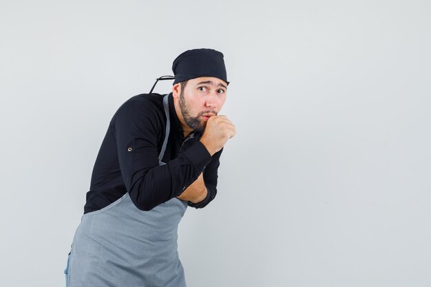 Young male suffering from cough in shirt, apron and looking sick , front view.