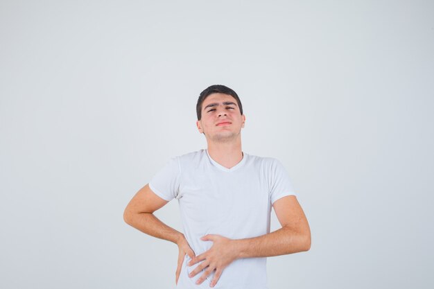 Young male suffering from liverache in t-shirt and looking painful , front view.