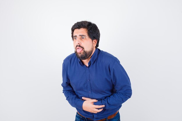 Young male suffering from stomach pain in blue shirt and looking unwell , front view.