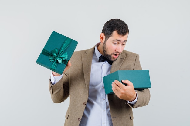 Young male in suit looking into present box and looking amazed , front view.