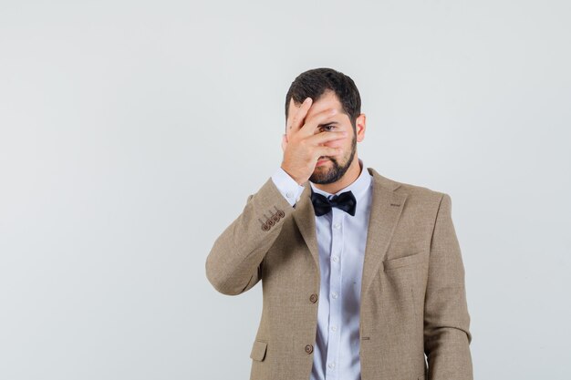 Young male in suit looking through fingers and looking timid , front view.