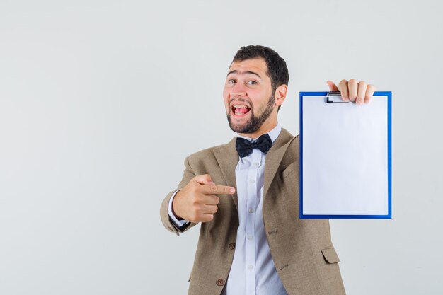 Young male in suit pointing at clipboard and looking cheery , front view.