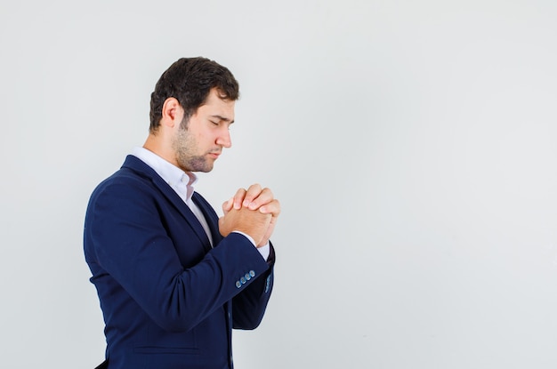 Young male in suit praying with clasped hands and looking hopeful.