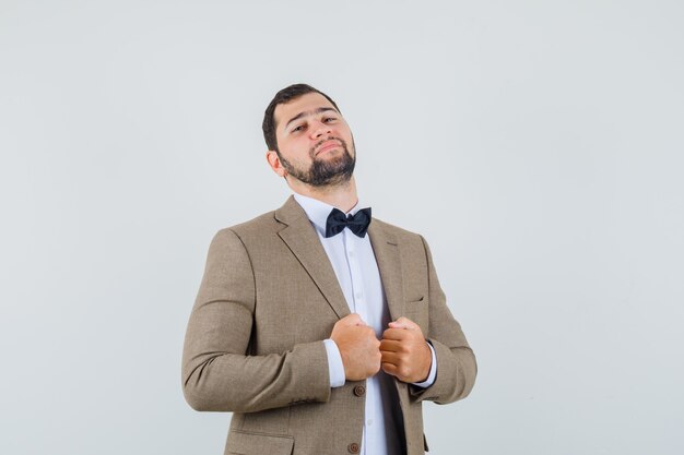 Young male in suit pulling collar of his jacket and looking confident , front view.