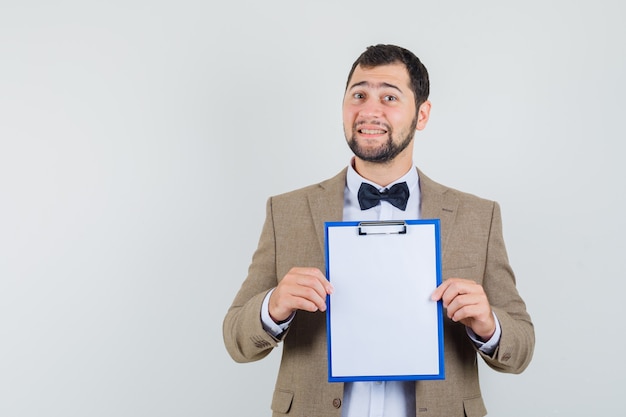 Free photo young male in suit showing clipboard and looking cheerful , front view.