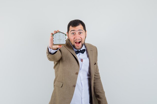 Young male in suit showing house model while screaming , front view.