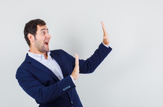 Young male in suit showing stop gesture by pushing himself and looking scared , front view.