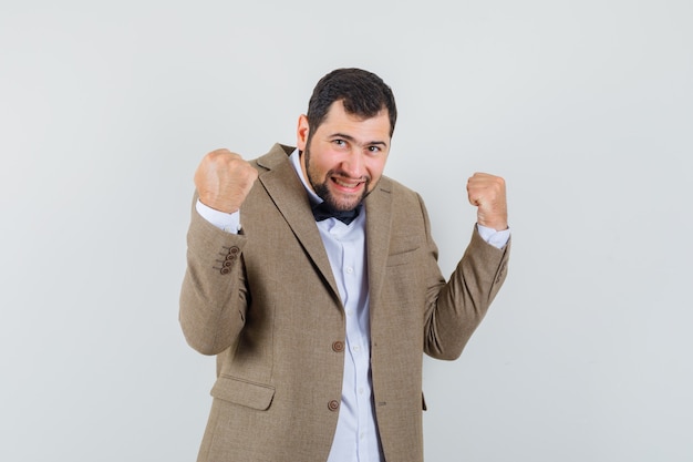 Free photo young male in suit showing winner gesture and looking lucky , front view.