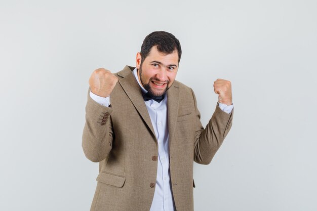 Young male in suit showing winner gesture and looking lucky , front view.