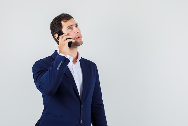 Young male in suit thinking while talking on smartphone and looking serious , front view.