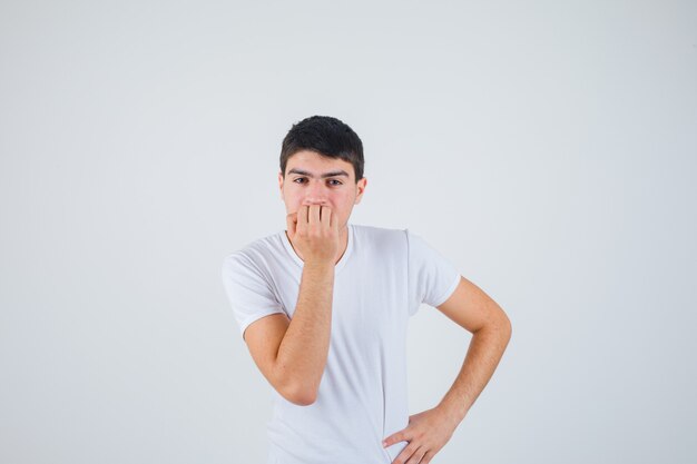 Young male in t-shirt biting him nails and looking thoughtful , front view.