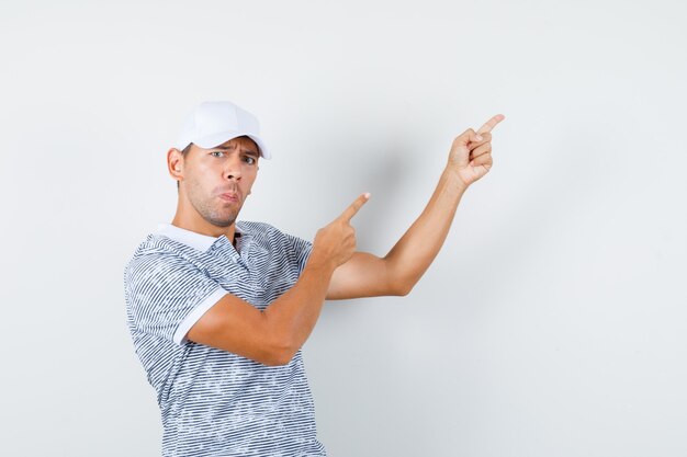 Young male in t-shirt and cap pointing fingers up and looking curious