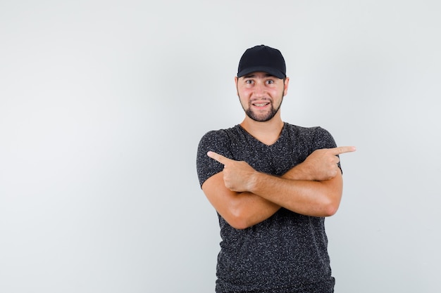 Young male in t-shirt and cap pointing to side and looking cheerful