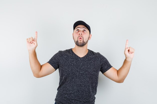 Young male in t-shirt and cap pointing up and looking focused