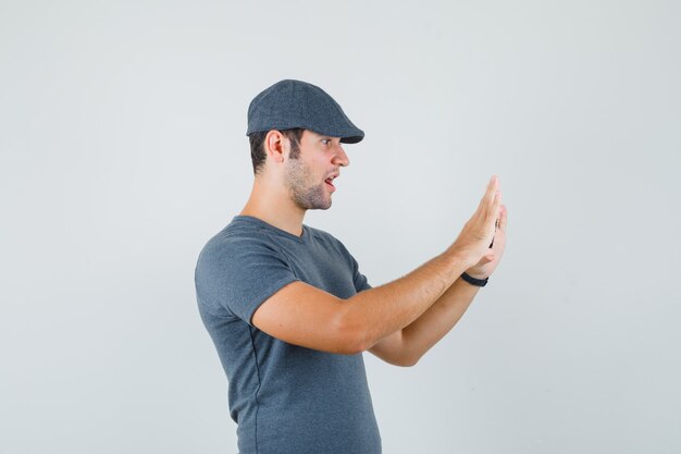 Young male in t-shirt cap taking photo on mobile phone and looking amazed  