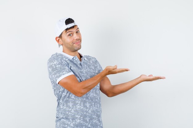 Young male in t-shirt and cap welcoming or showing something and looking glad