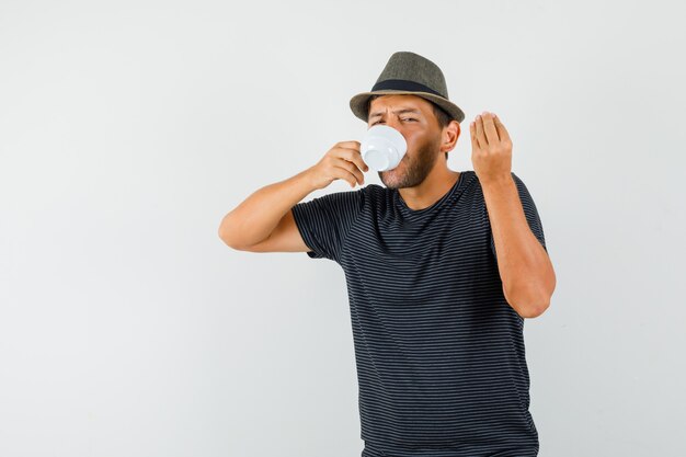 Young male in t-shirt hat drinking coffee doing italian gesture and looking delighted  