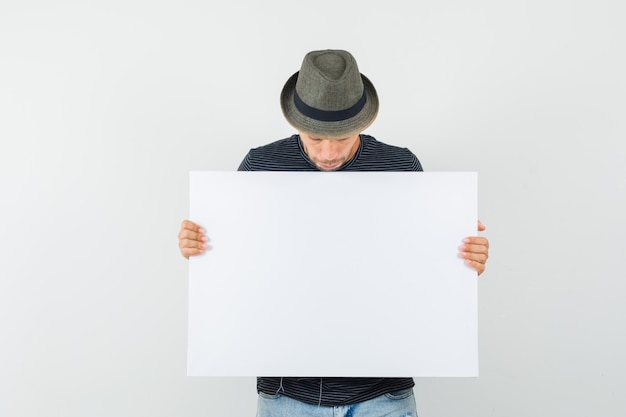 Free photo young male in t-shirt hat jeans looking at blank canvas and looking focused