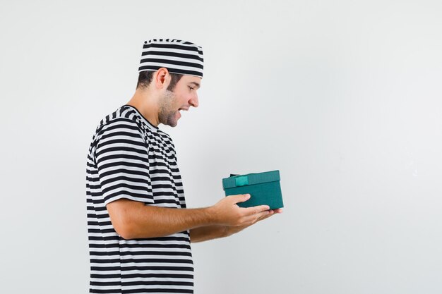 Young male in t-shirt, hat looking at gift box and looking focused .