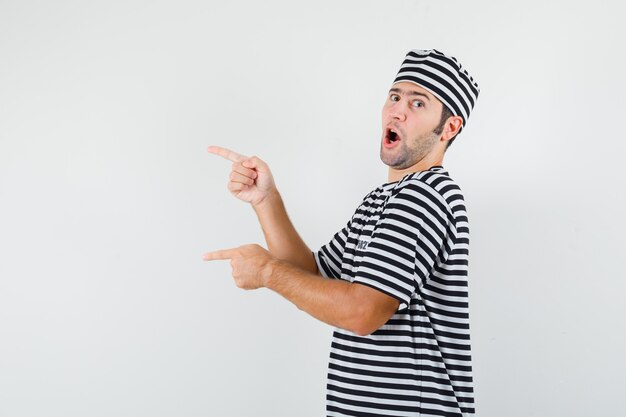 Young male in t-shirt, hat pointing to the left side and looking confident .