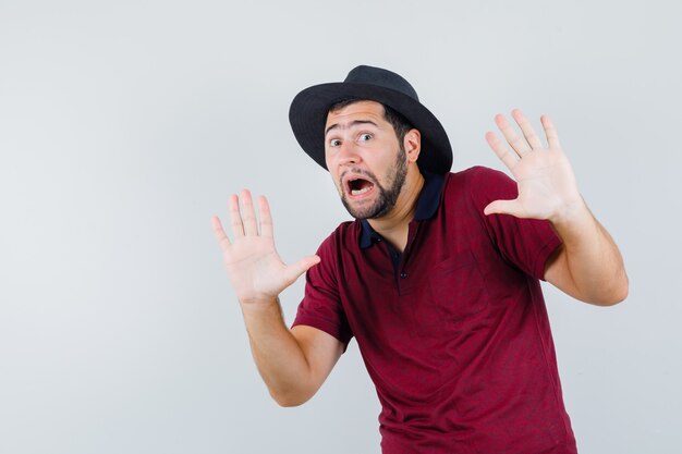 Young male in t-shirt,hat showing helpless gesture and looking scared , front view.