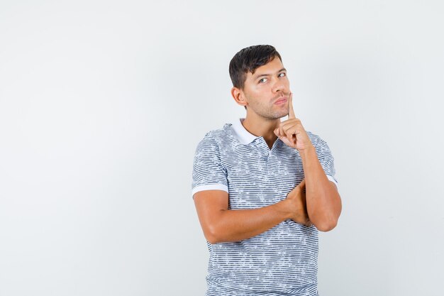 Young male in t-shirt holding finger near mouth and looking pensive