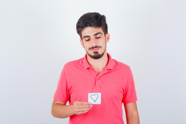 Young male in t-shirt holding sticky note while looking down and looking hopeful , front view.