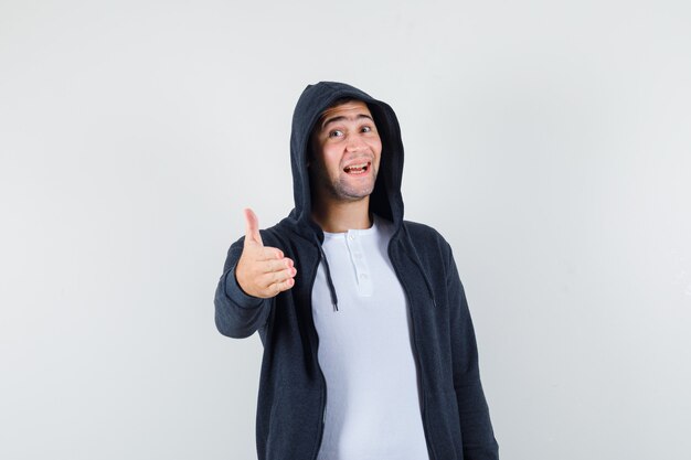 Молодой мужчина в футболке, пиджаке дает руку для тряски и выглядит веселым, вид спереди.