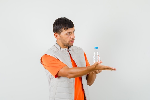 Young male in t-shirt, jacket holding bottle of water, stretching out hand , front view.