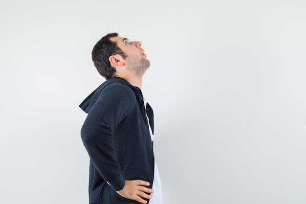 Young male in t-shirt, jacket holding hands on waist and looking focused .