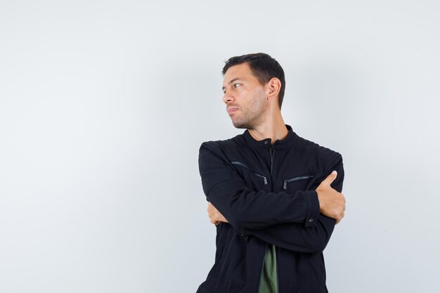 Young male in t-shirt, jacket looking aside with crossed arms and looking elegant , front view.