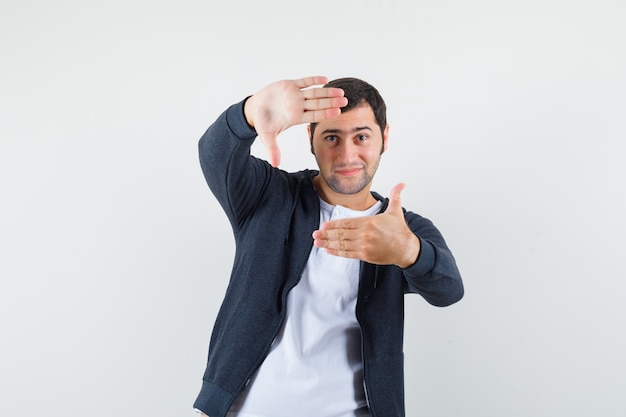 Young male in t-shirt, jacket making frame gesture and looking glad , front view.