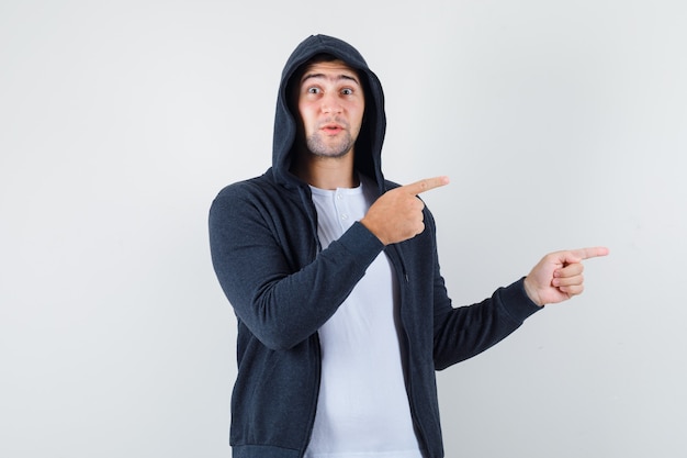 Young male in t-shirt, jacket pointing aside and looking puzzled , front view.