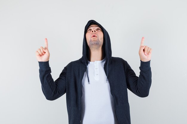 Young male in t-shirt, jacket pointing up and looking grateful , front view.