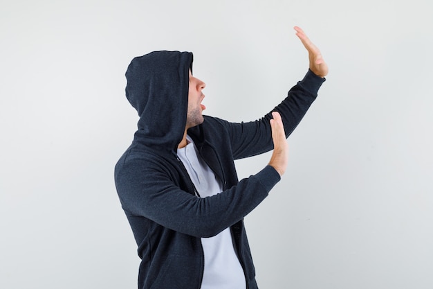 Молодой мужчина в футболке, куртка поднимает руки, чтобы защитить себя и выглядит испуганным, вид спереди.