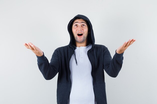 Young male in t-shirt, jacket raising hands, looking up and looking happy , front view.