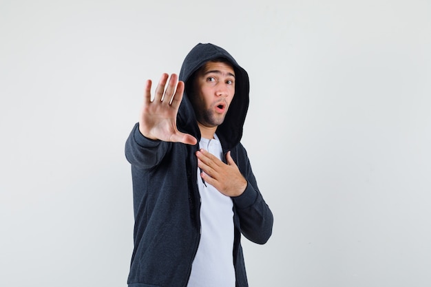 Young male in t-shirt, jacket showing stop gesture and looking scared , front view.