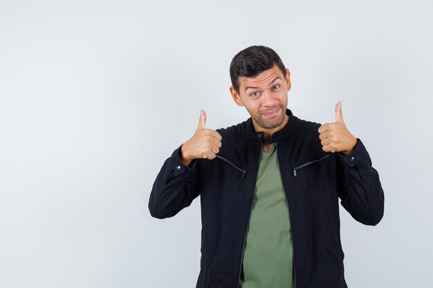 Young male in t-shirt, jacket showing thumbs up and looking cheerful , front view.