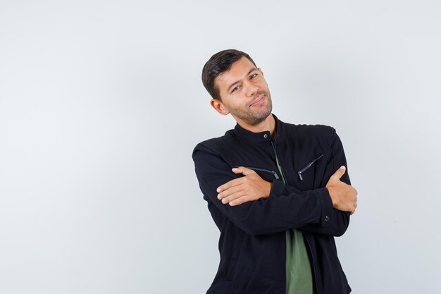 Young male in t-shirt, jacket standing with crossed arms and looking cheerful , front view.