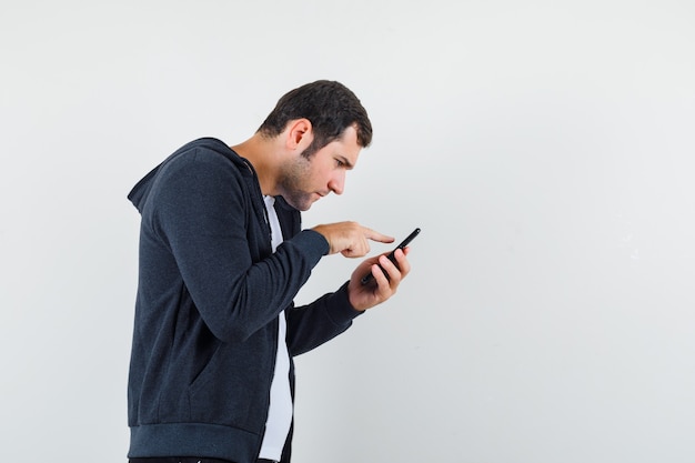 Young male in t-shirt, jacket using mobile phone and looking focused .