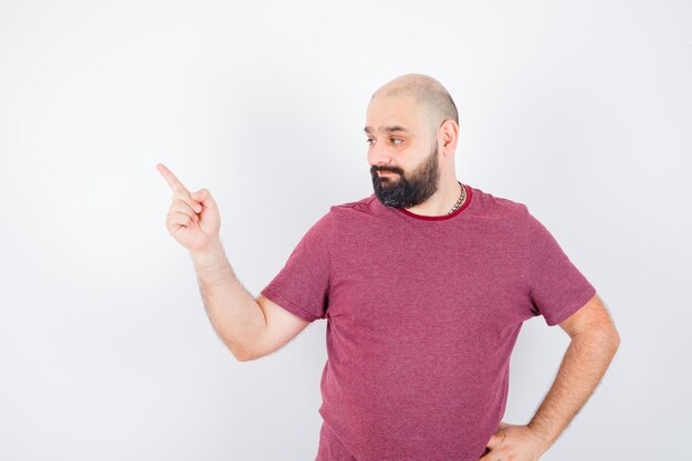 Young male in t-shirt pointing aside and looking confident , front view.