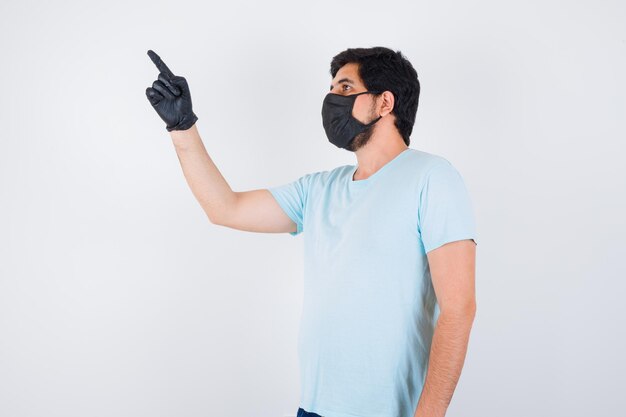 Young male in t-shirt pointing at upper left corner and looking focused , front view.