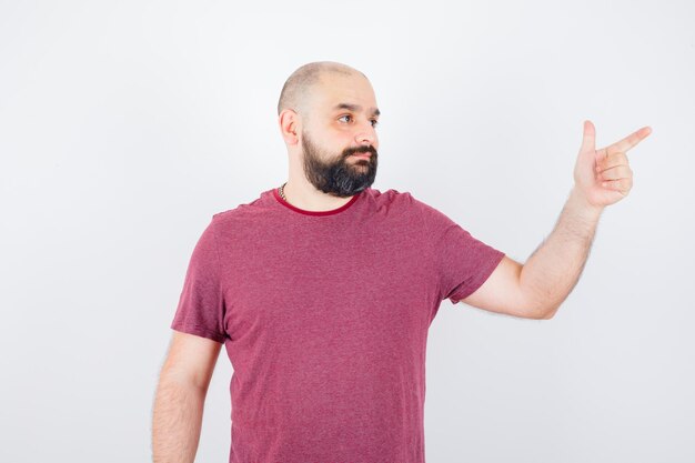 Young male in t-shirt pointing at upper right corner and looking focused , front view.