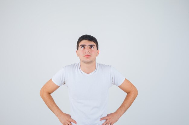 Young male in t-shirt posing with hands on waist and looking pensive , front view.