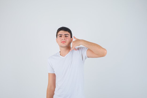 Young male in t-shirt showing phone gesture and looking self-confident , front view.