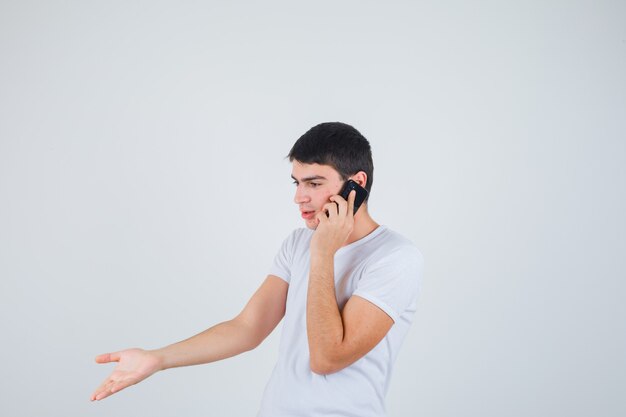 Молодой мужчина в футболке разговаривает по мобильному телефону и выглядит взволнованным, вид спереди.