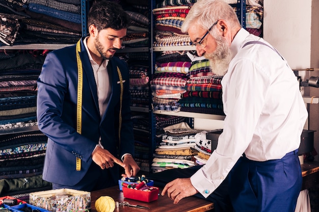 Young male tailor showing colorful spool to his customer in the shop