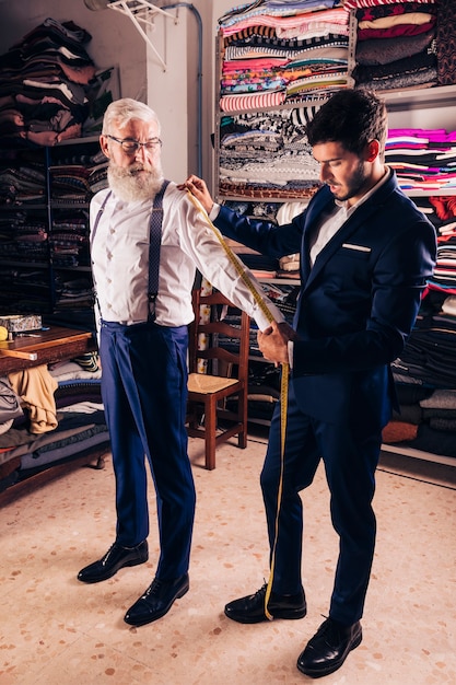 店で年配の男性の袖の測定を取る若い男性テーラー