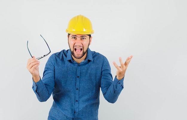 Young male taking off glasses while screaming in shirt