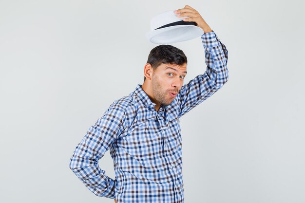 Young male taking off his hat in checked shirt and looking
glad